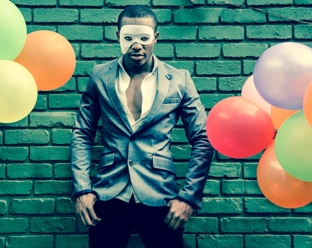 man in blue button up jacket and black pants standing beside wall with balloons